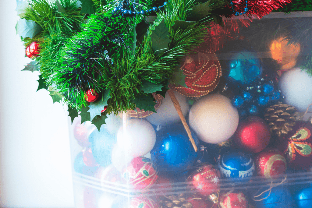 A clear container holding various Christmas ornaments and a Christmas wreath. 