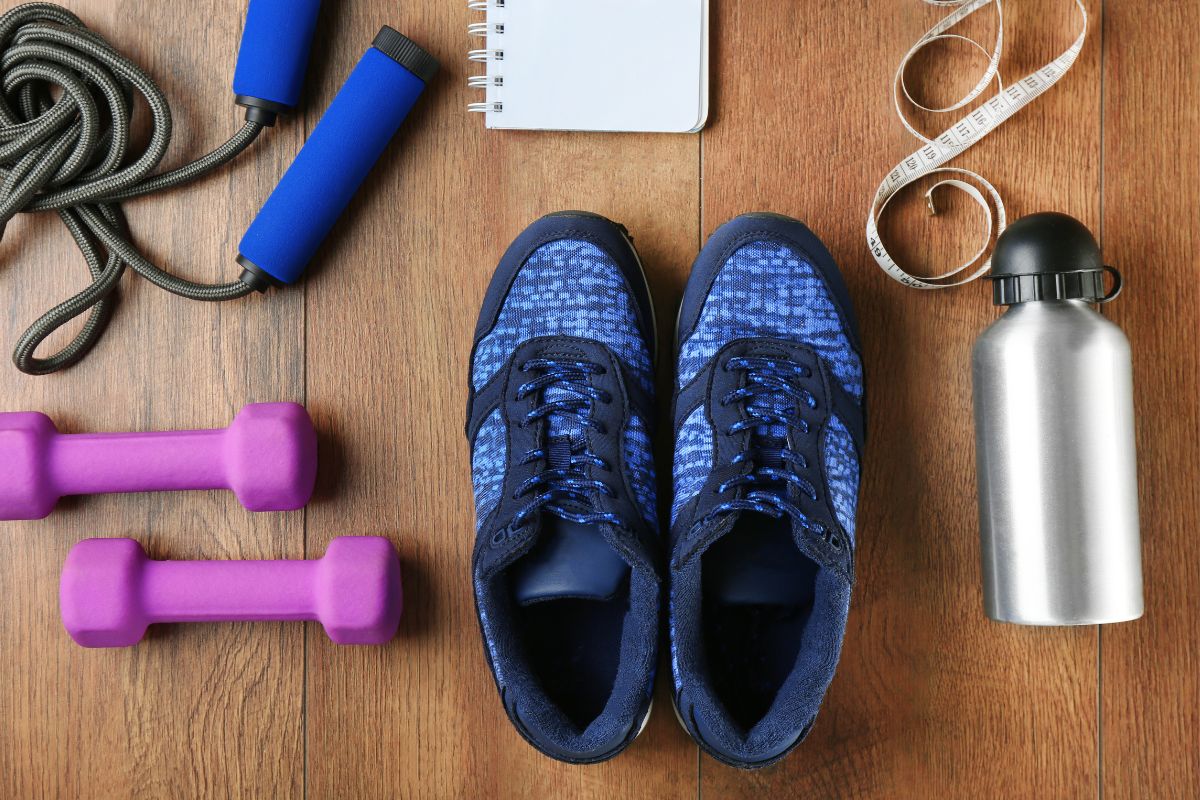 Workout gear laid out on a wooden floor including shoes, hand weights, and a jump rope.