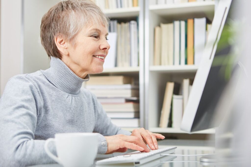 An older woman smiling and looking at a computer. 