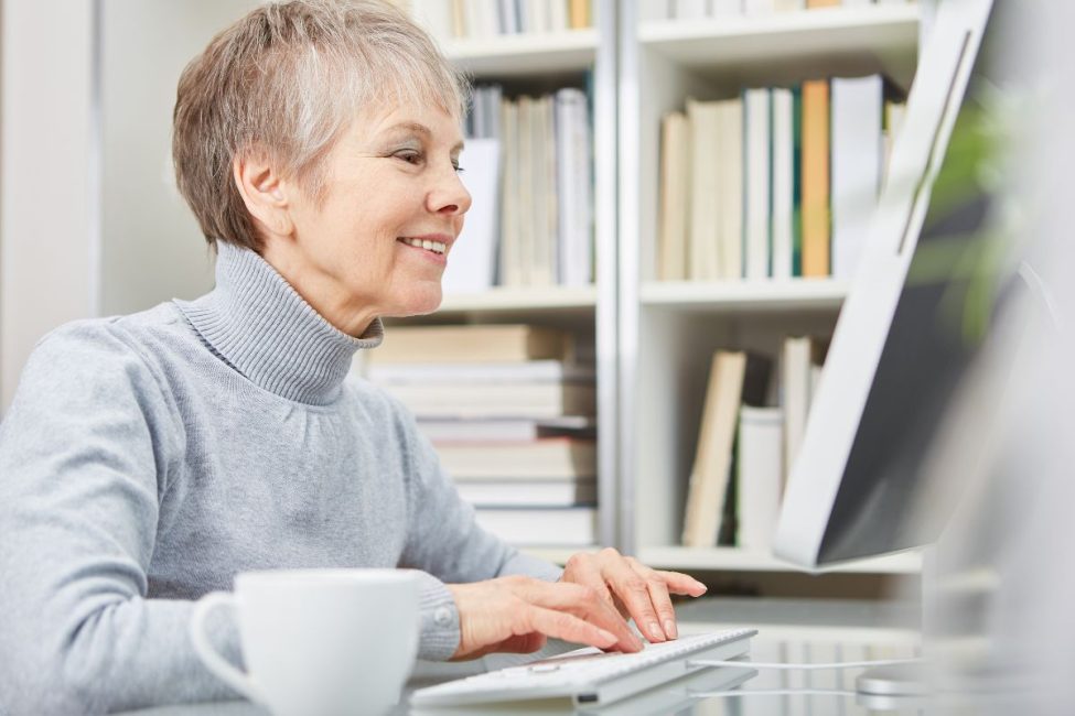 An older woman smiling and looking at a computer.
