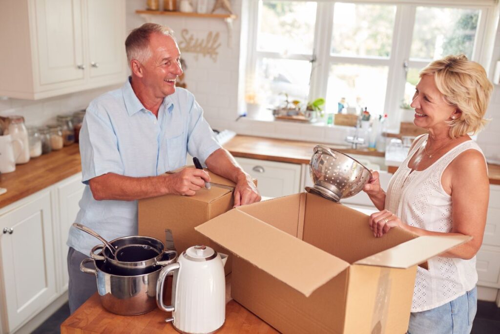 An older couple putting items in boxes while standing in a kitchen.