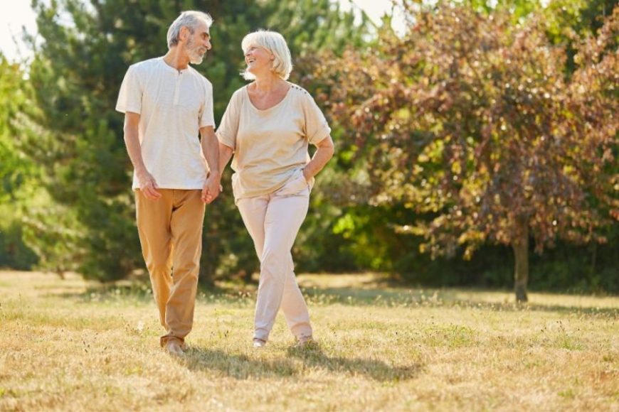 An elderly couple walking hand in hand outside.