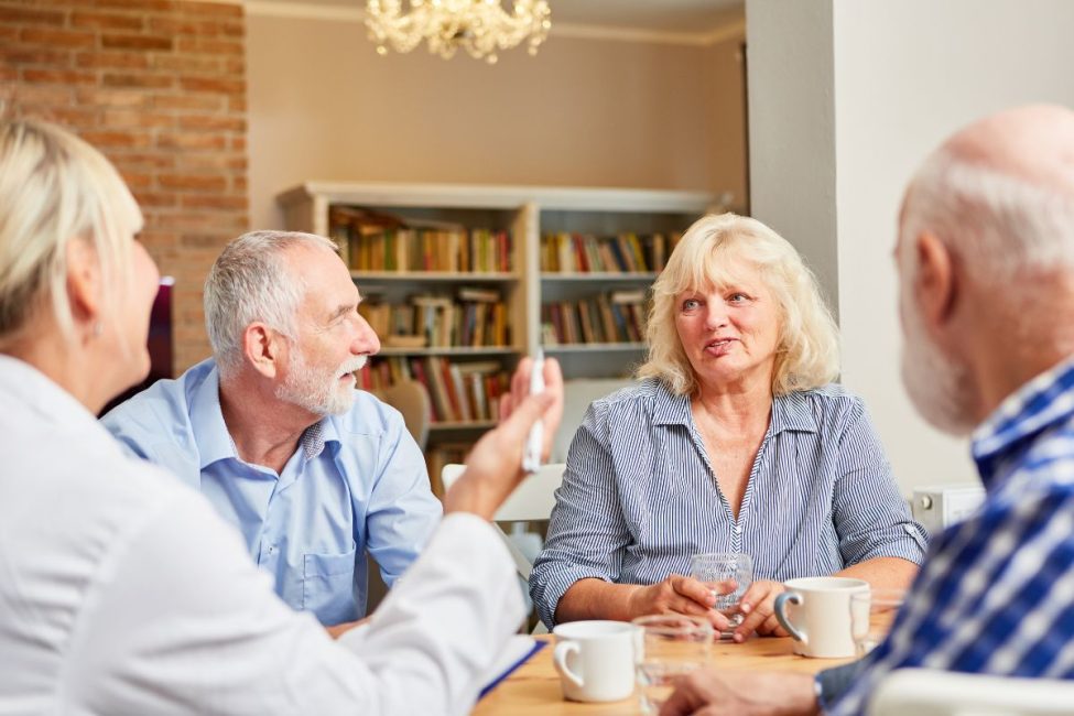 Four middle aged people having a conversation around a table.