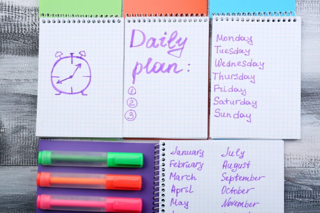 Notebooks lined up with different tasks on each one including a daily plan, the days of the week, and each month of the year in purple writing. 