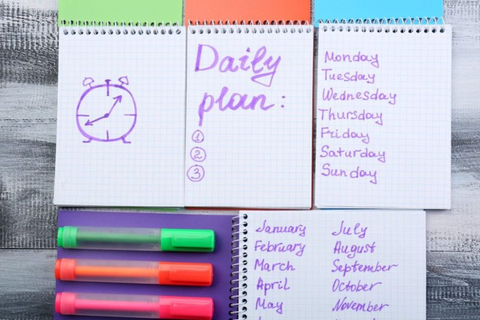 Notebooks lined up with different tasks on each one including a daily plan, the days of the week, and each month of the year in purple writing.