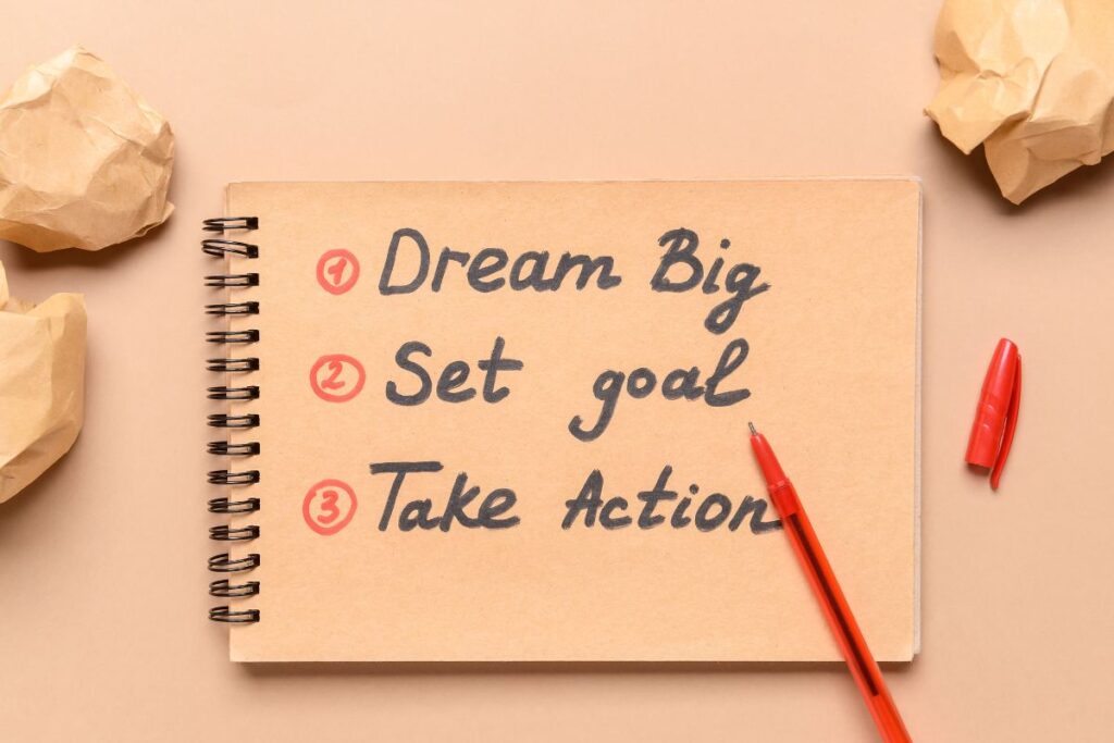 A brown paper notebook on a brown background with three numbered bullets, including "dream big," "set goal," and "take action."