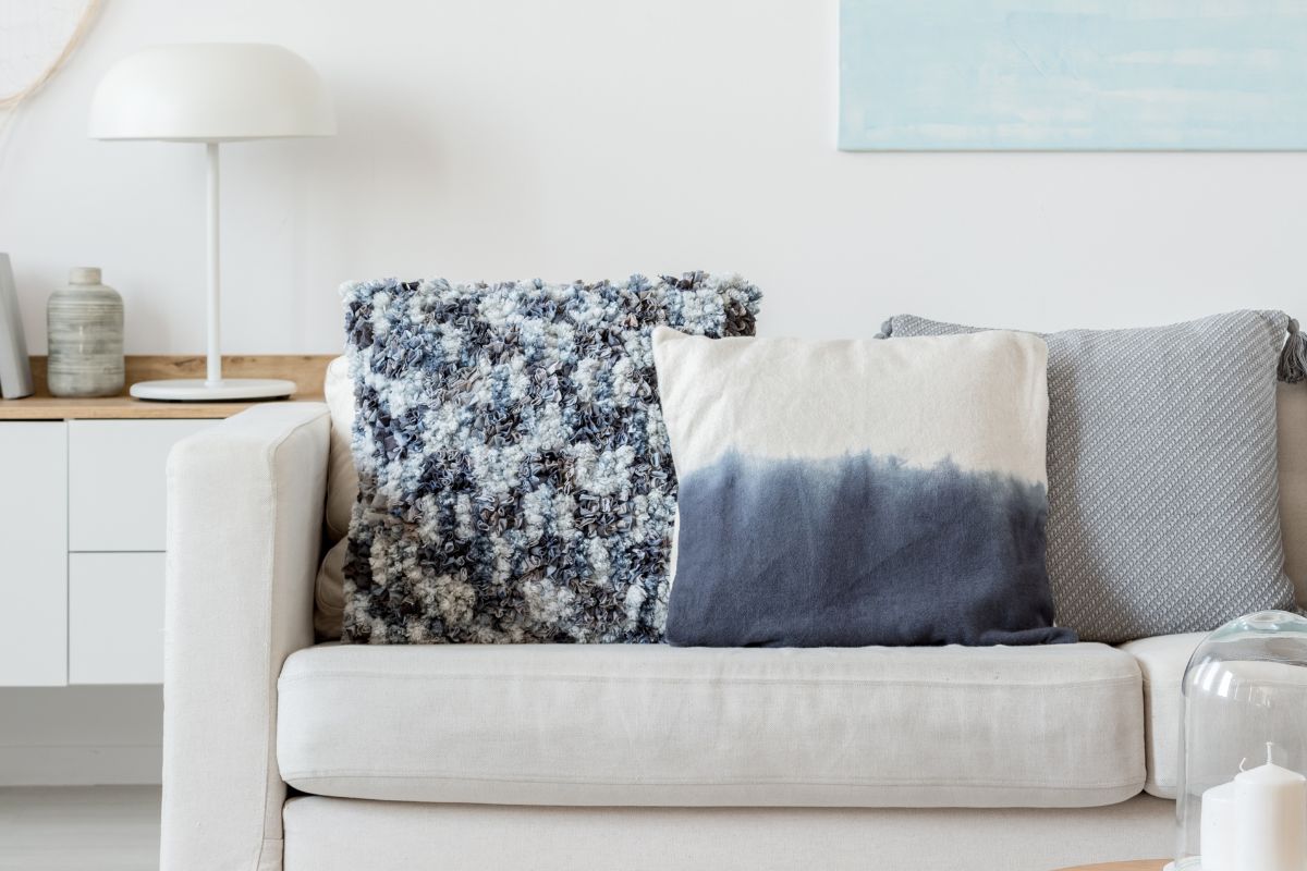 A grey couch with white and navy blue decretive pillows on it with modern furniture and paintings behind it.