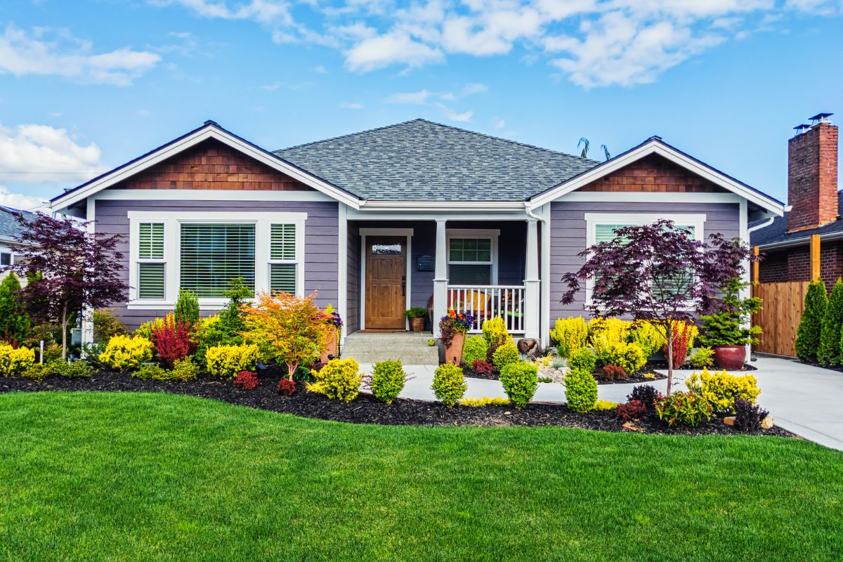 The exterior of a grey one story home with green grass and colorful landscaping.