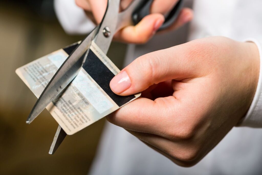 A close up of someone cutting a credit card in half with a pair of metal scissors. 