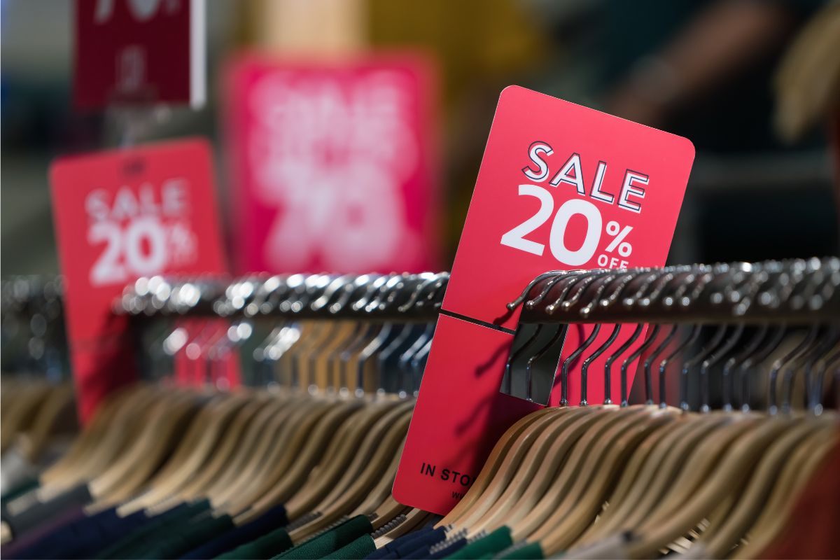 A close up picture of a red sign on top of a clothing rack at a store that says "SALE 20% off."