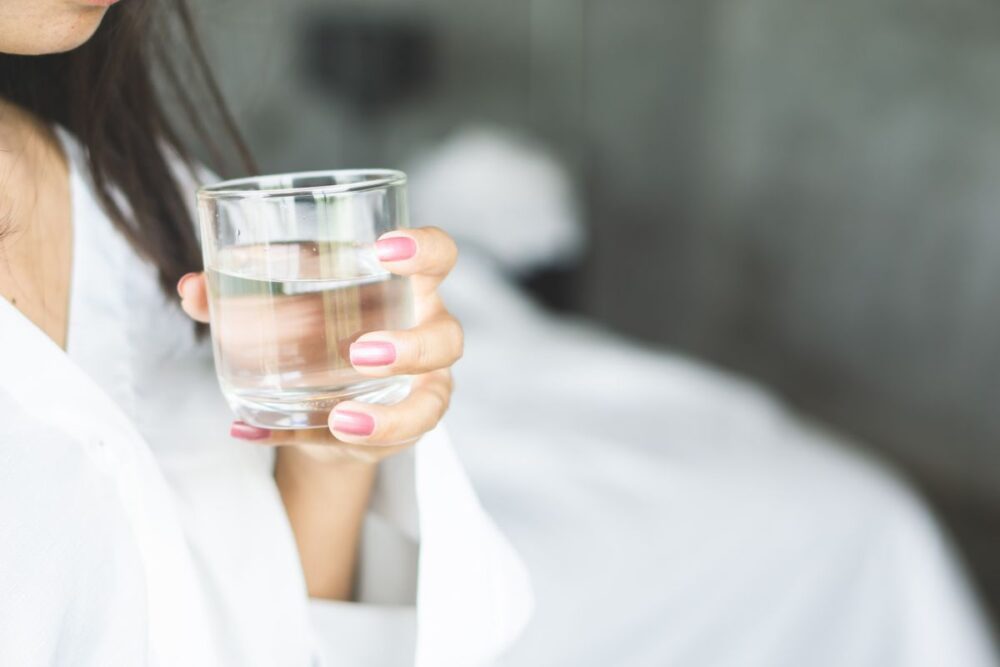 A close up picture of a small glass of water being held by a woman in a white robe.