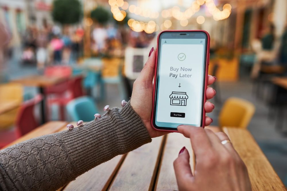 A woman holding a phone with the words "Buy Now, Pay Later" on the phone screen.