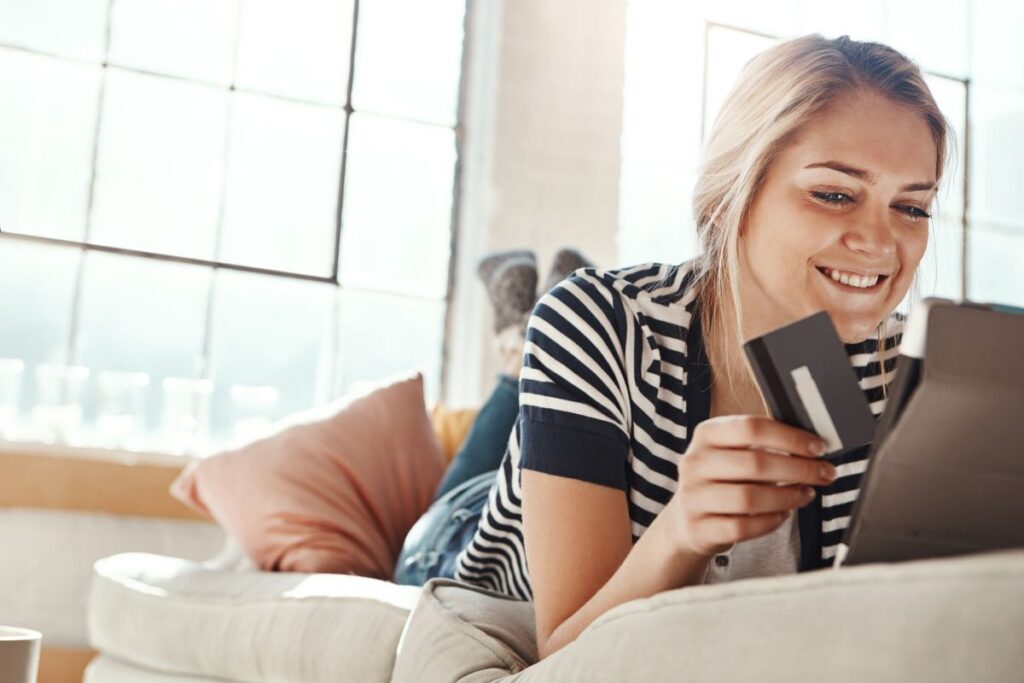 A woman holding a credit card and smiling as she looks at the screen of a laptop in front of her