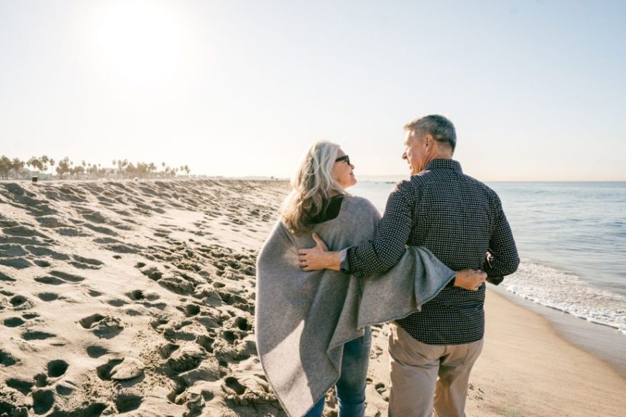 A man and woman walking down the beach as they hold each other and look in each other's eyes.