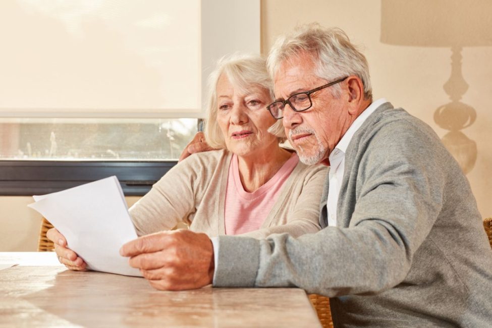 A man and woman embracing as they look at a piece of paper together and sit at a table.