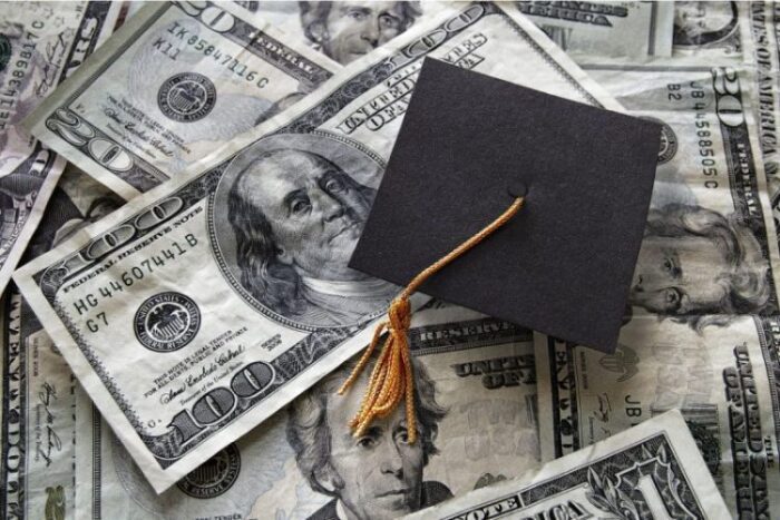 A graduation cap sitting on top of money spread out.