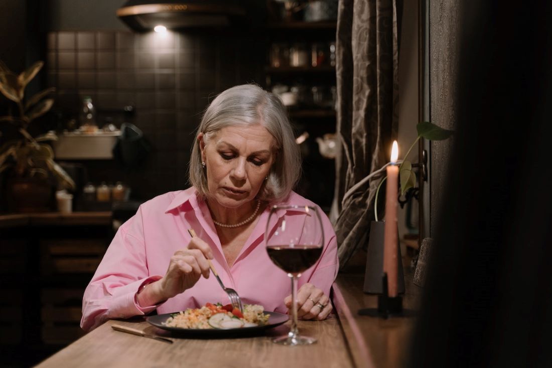 older woman pint shirt eating dinner alone