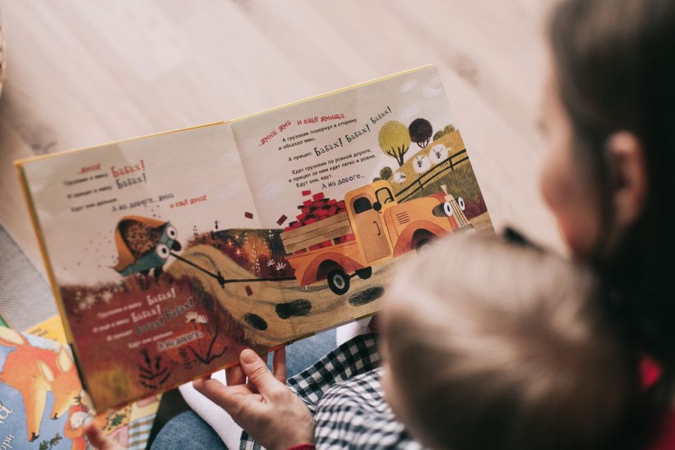 A mom reading a colorful children's book with her young child on her lap.