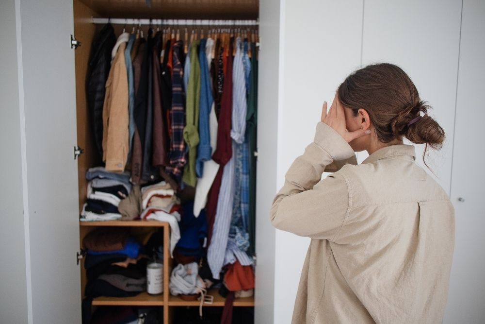 A messy closet and a girl staring at it with her hands on her face