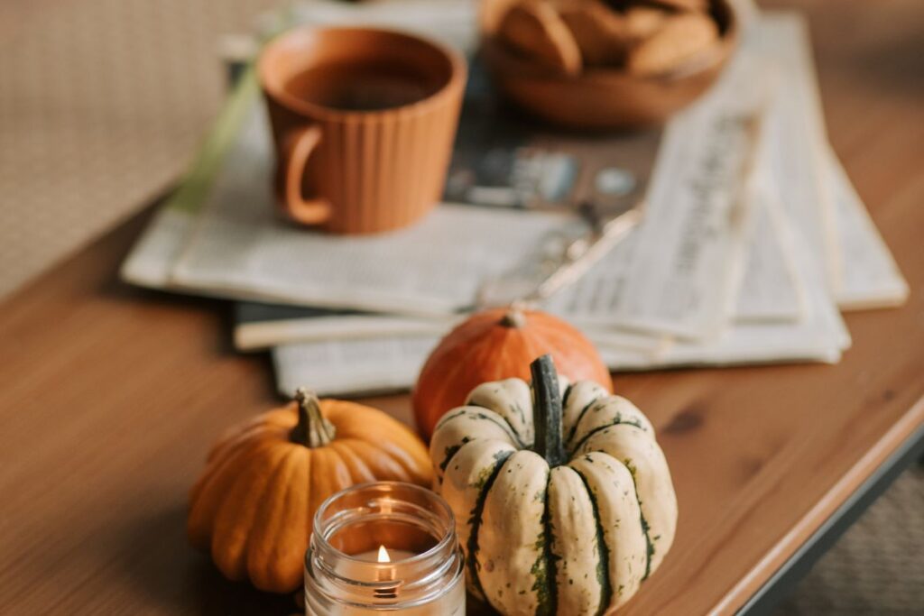 A cozy coffee table with fall decorations, pumpkins and candles, with a mug and newsletters in the background.