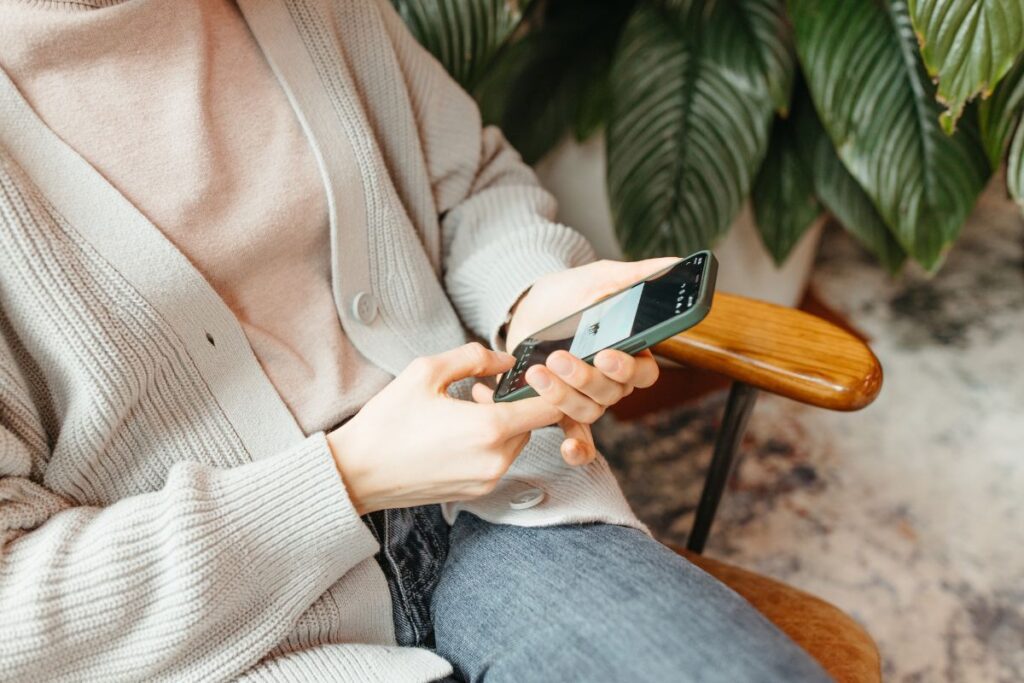 A woman sitting in a wooden chair looking at her phone.