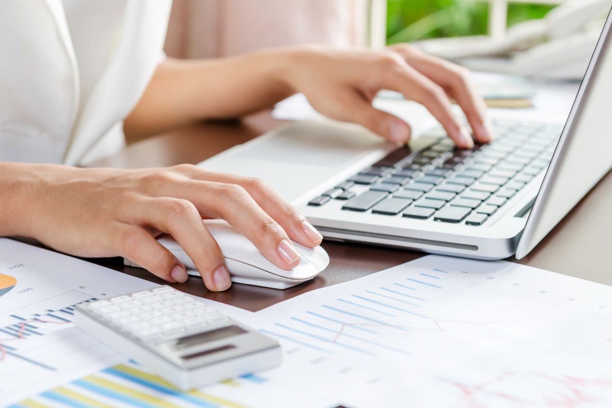 A woman with one hand on a laptop keyboard and the other hand on a wireless mouse.