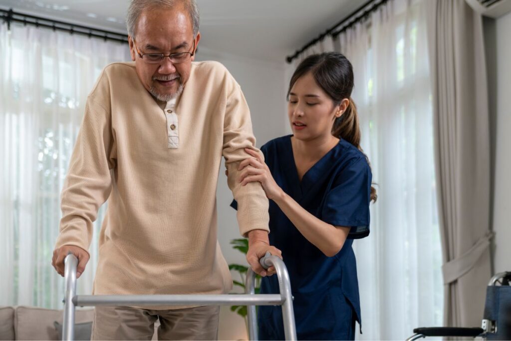 An elderly man walking with a walker and a nurse holding onto his arm to help him. 