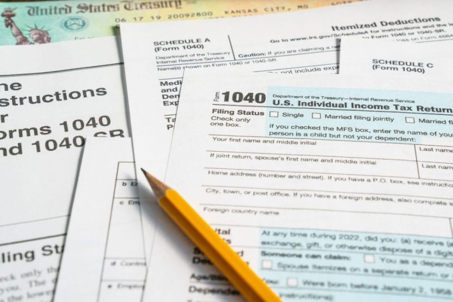 Tax forms, like 1040, stacked on top of each other with a pencil.