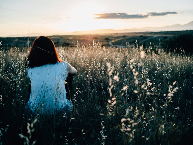 woman sitting in field watching sunset