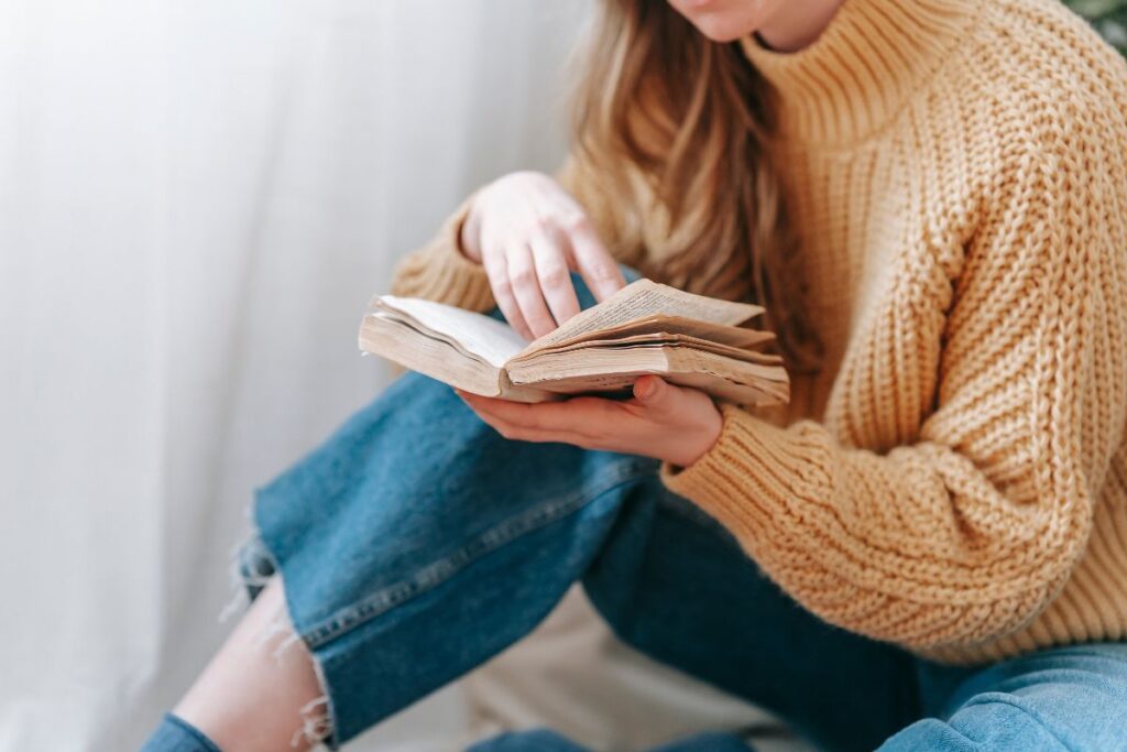 woman in jean and sweater reading a book