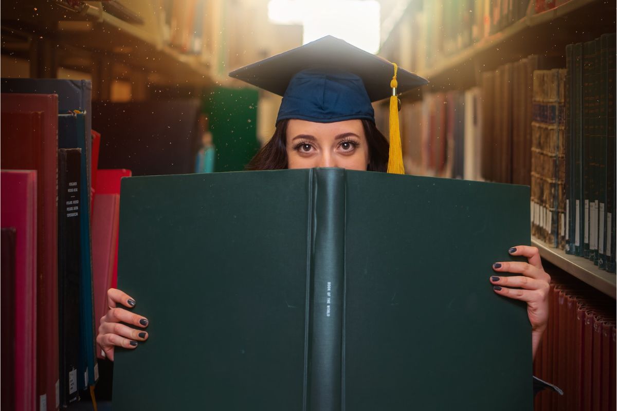 college graduate hiding behind book