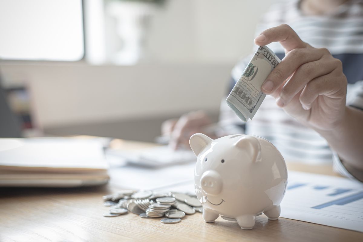 A person putting money into a small white piggy bank.