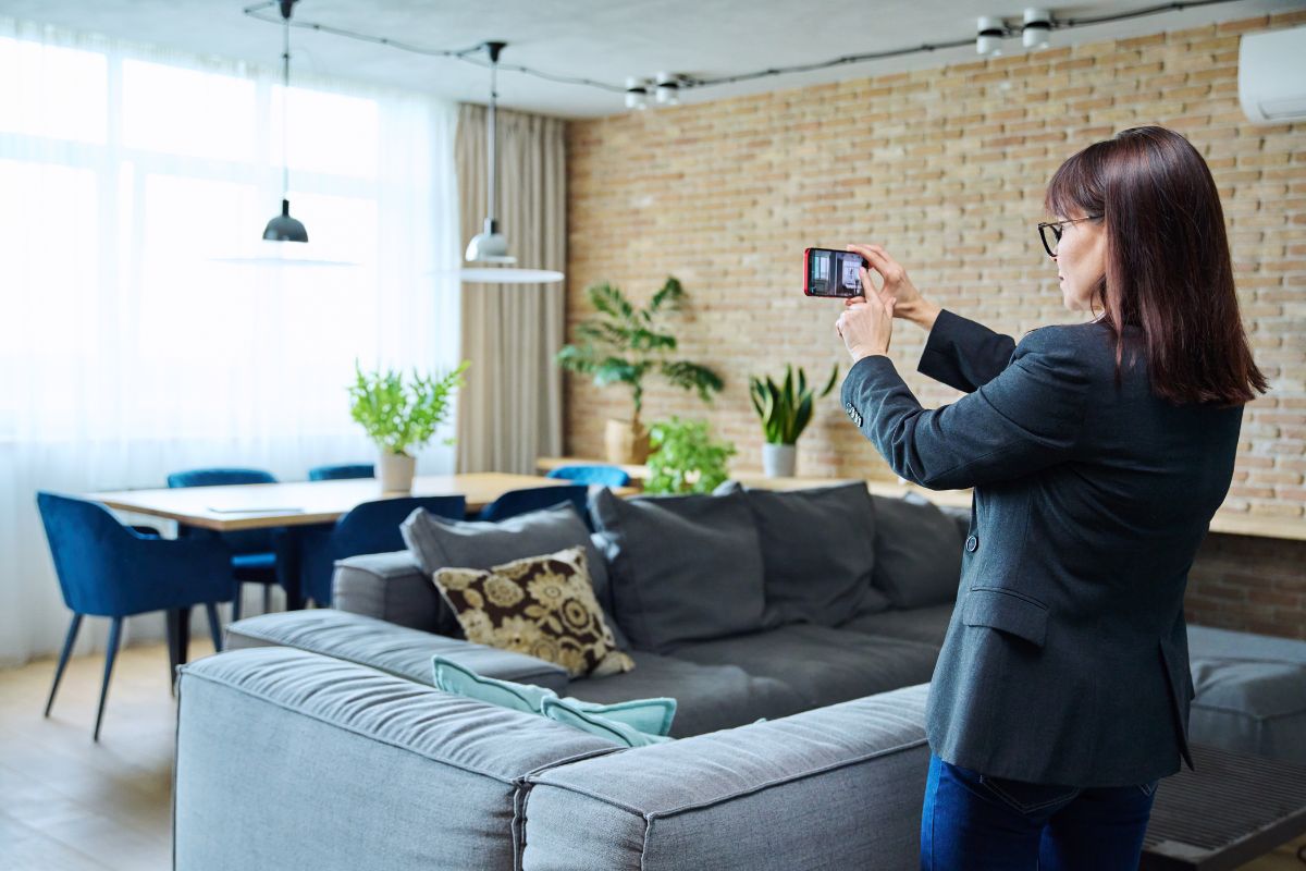 A woman in a suit and taking a picture of a dining room on a smartphone.