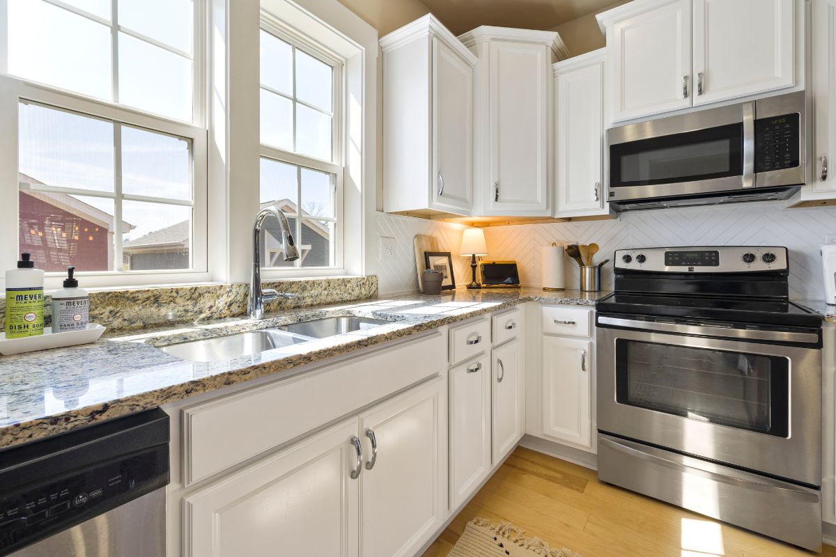A closeup photo of a kitchen with white cabinets and stainless steel appliances.
