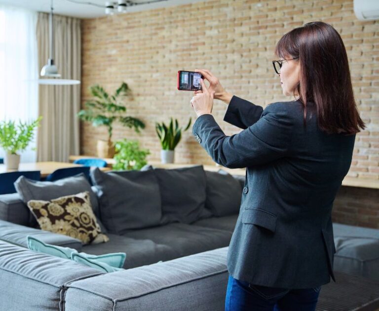 Woman in a pantsuit holding her phone out to take a picture of her dining room for a home inventory.