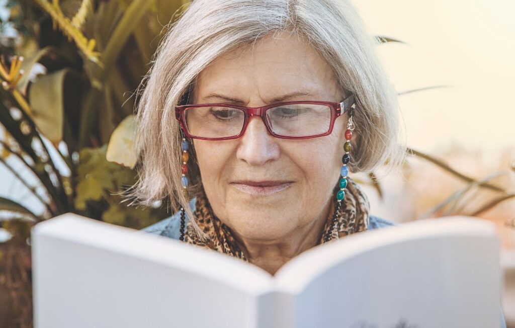 An older woman reading a book in the summer. 