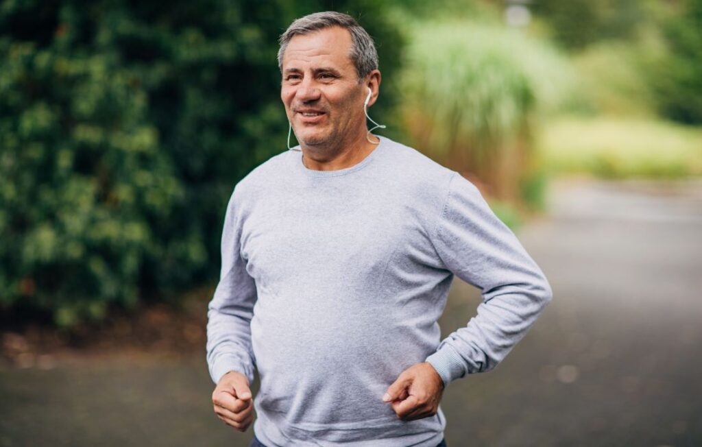 An older man exercising outside while listening to an audiobook in ear buds. 