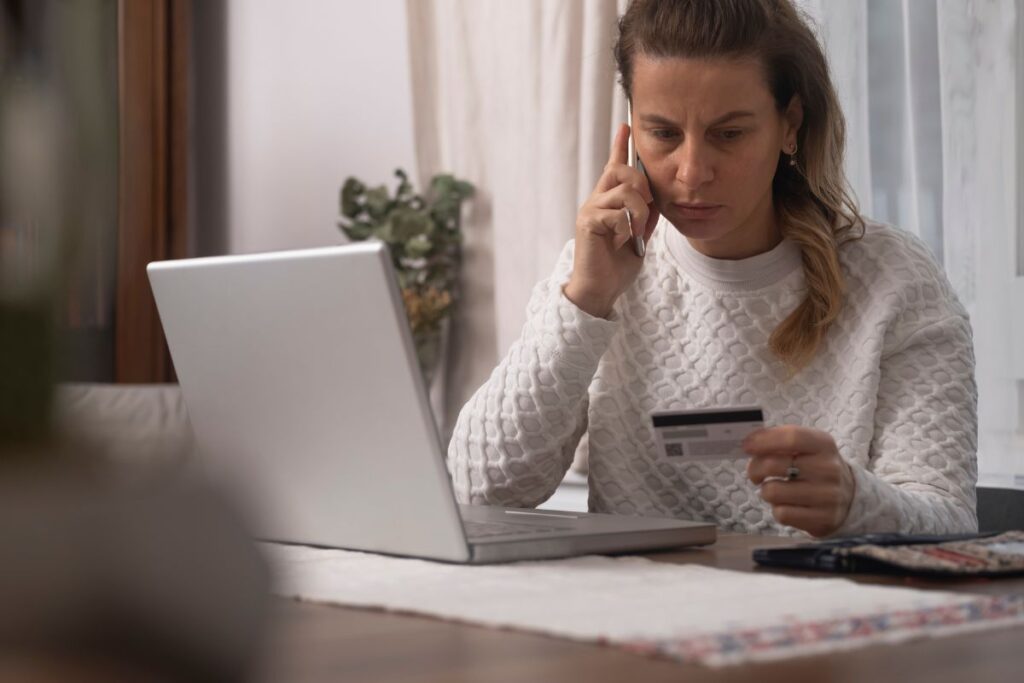 A woman talking on her phone while looking at her credit card and trying to escape a financial scam. 