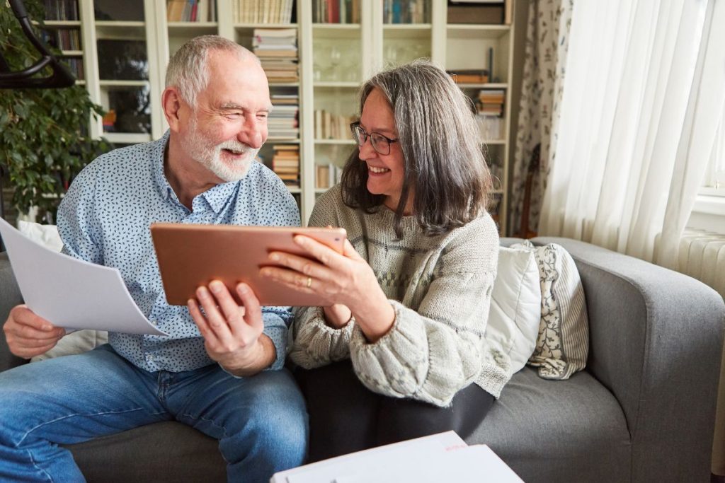 An older couple smiling and looking at a tablet